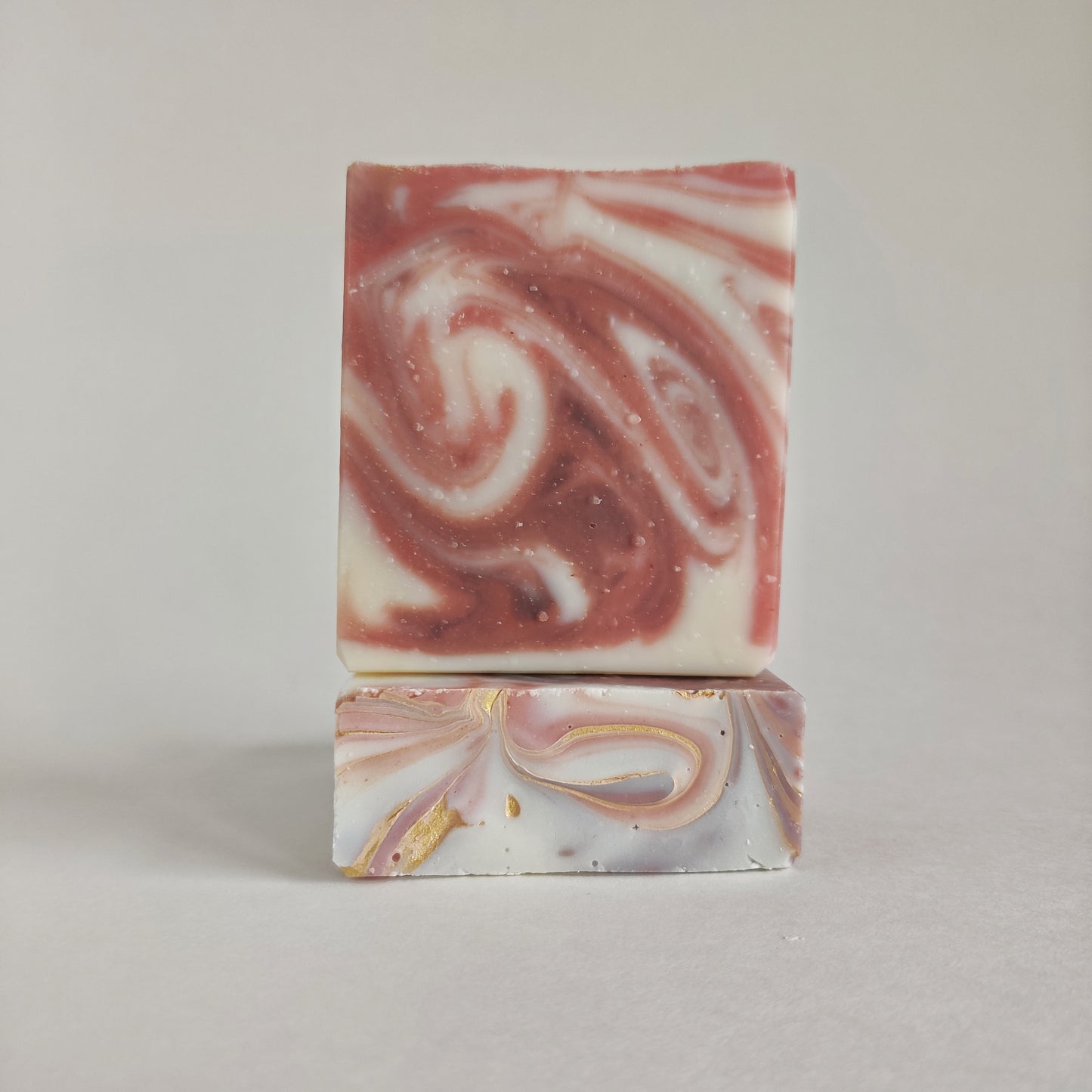 Product photo of two bars of soap from the front and top. The soap is decorated with pink, purple, and white swirls throughout. The top is decorated with additional gold swirls.